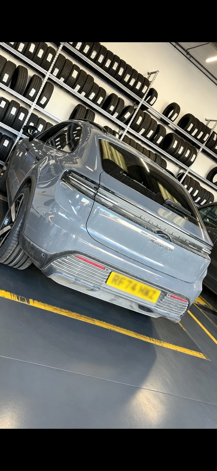 Grey Porsche Macan 4S in a workshop with walls of tyre stock behind it during a tyre change