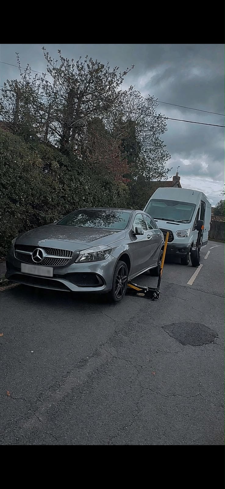 Silver Mercedes A-Class raised on a mobile trolley jack beside the Mobile Tyre Pros van on a village road in Prestwood